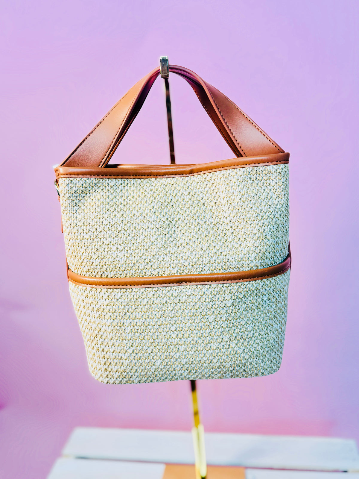 Woven cream and mint green market bag with brown leather handles and trim against purple background.
