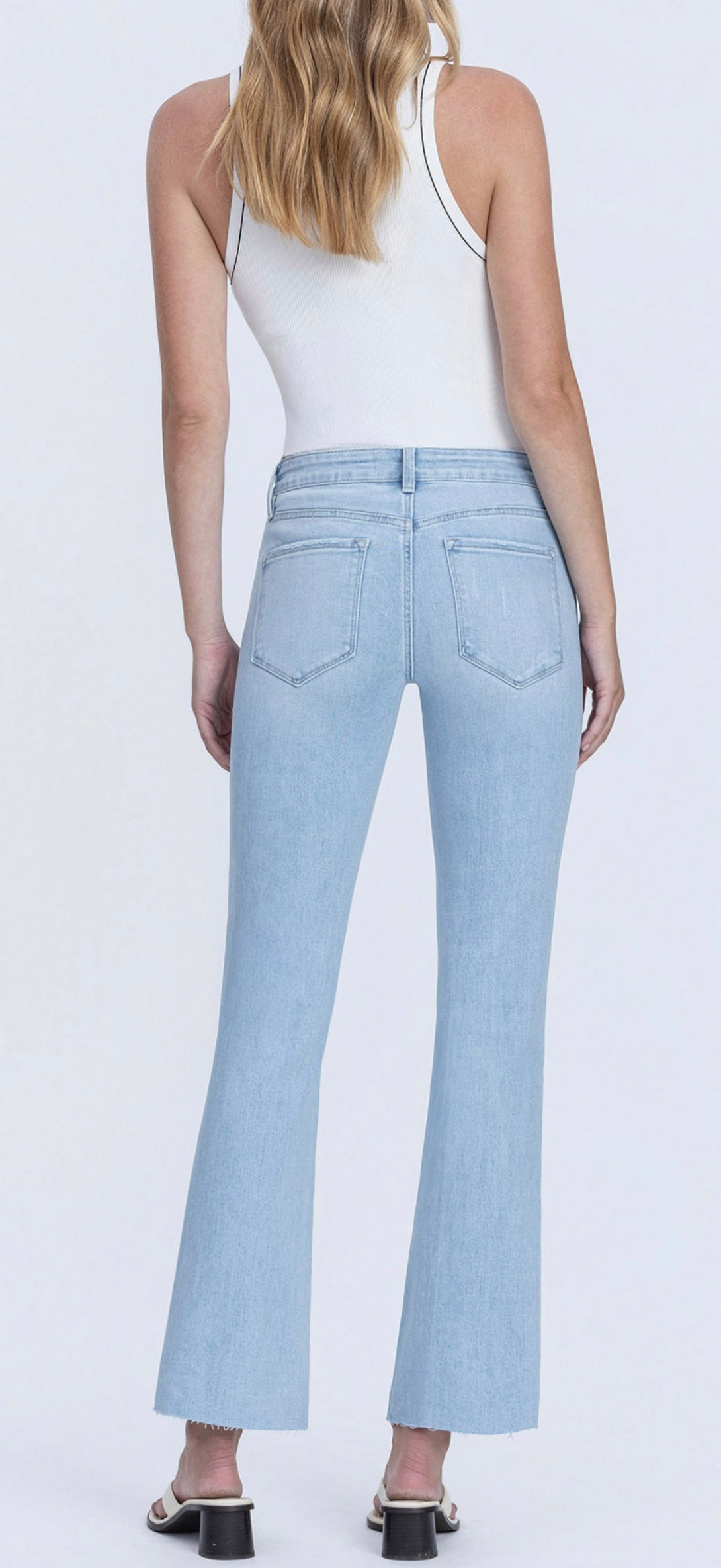 Back view of woman wearing light blue cropped flare jeans and white tank top