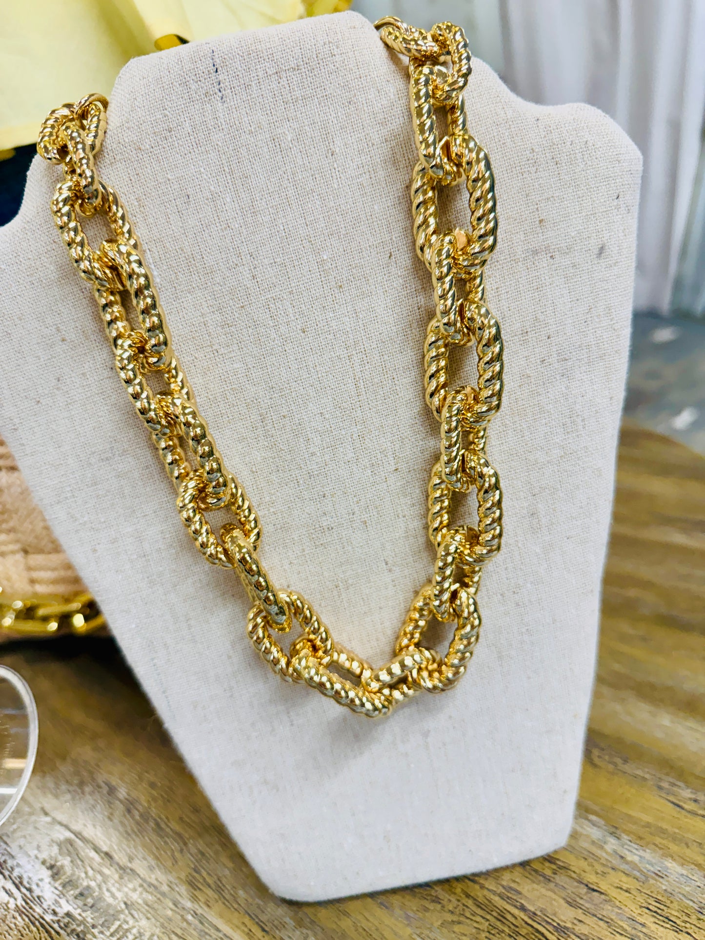 Bold gold twisted rope chain link necklace displayed on linen jewelry bust stand.