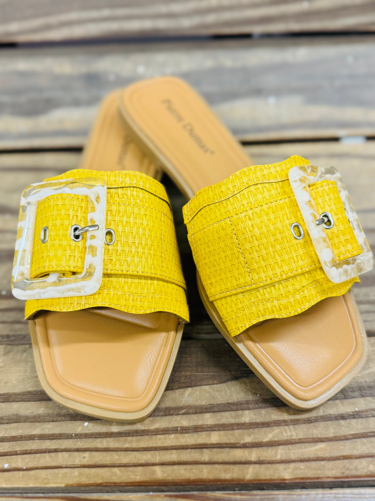 Yellow textured slide sandals with clear buckle straps and tan soles on wooden surface