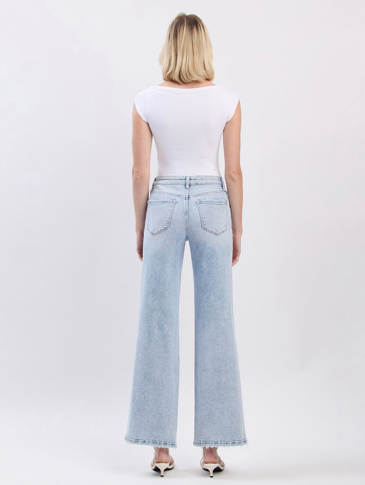 Back view of woman wearing light blue wide-leg Josephine denim jeans with white sleeveless top and heels.