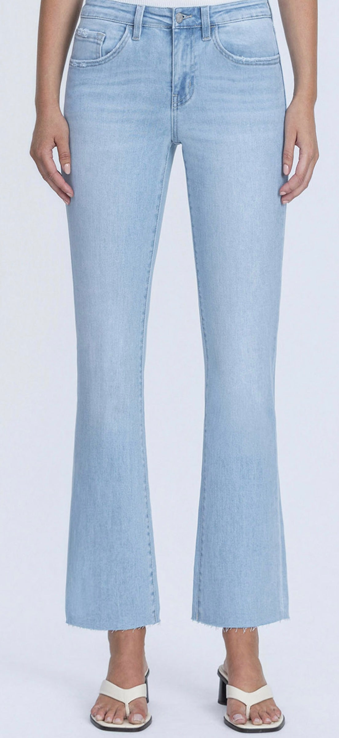 Light blue cropped flare jeans with frayed hem on model wearing white sandals