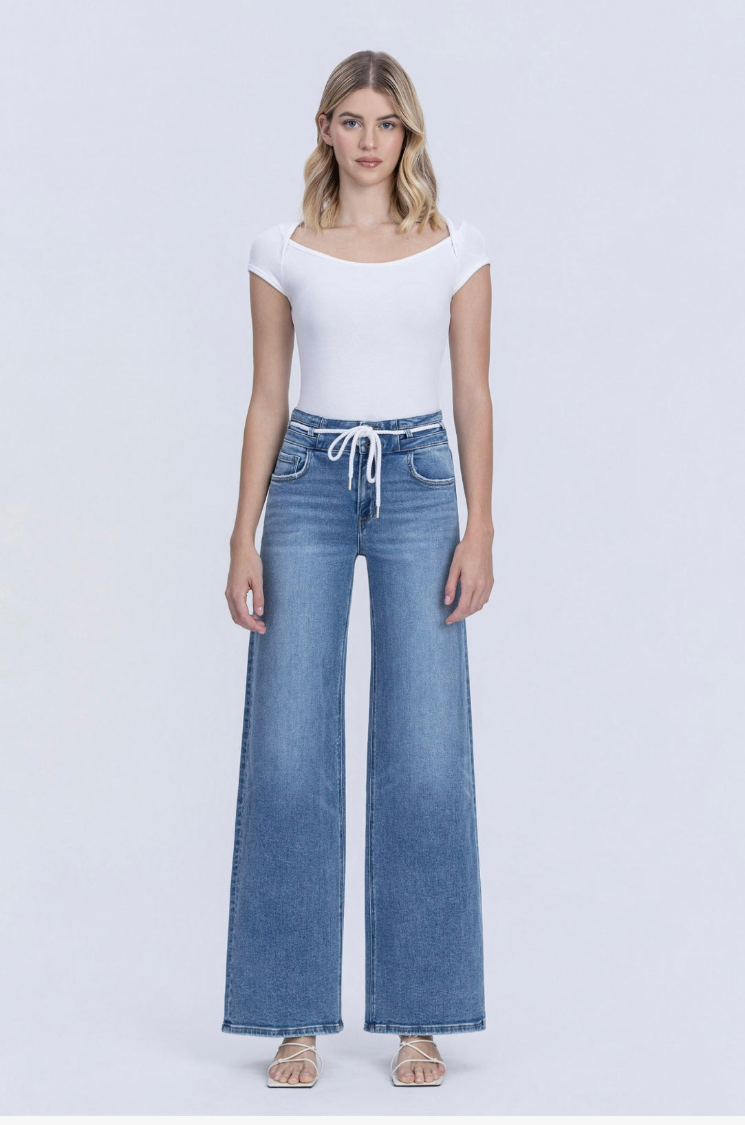 Woman wearing white top and medium wash wide-leg drawstring denim pants with white sandals