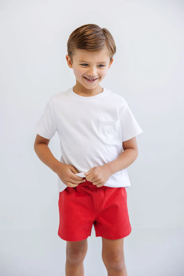 Young boy wearing white Carter crewneck t-shirt with chest pocket and red shorts, smiling at camera.