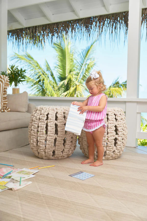 Young child in pink striped romper outfit standing on covered patio with tropical background