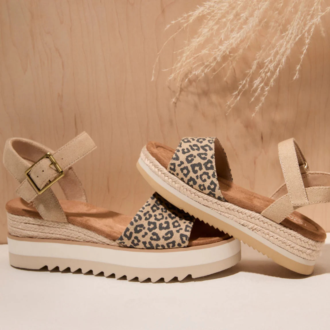 Two leopard print wedge sandals with espadrille soles and beige ankle straps on textured background.