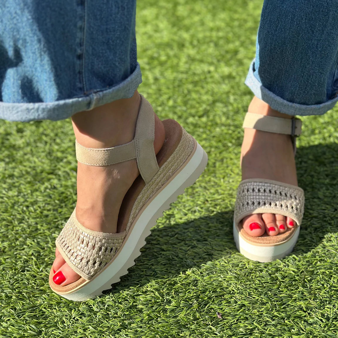 Woman wearing beige Diana wedge sandals with woven straps and ankle buckles on grass, red pedicure visible.