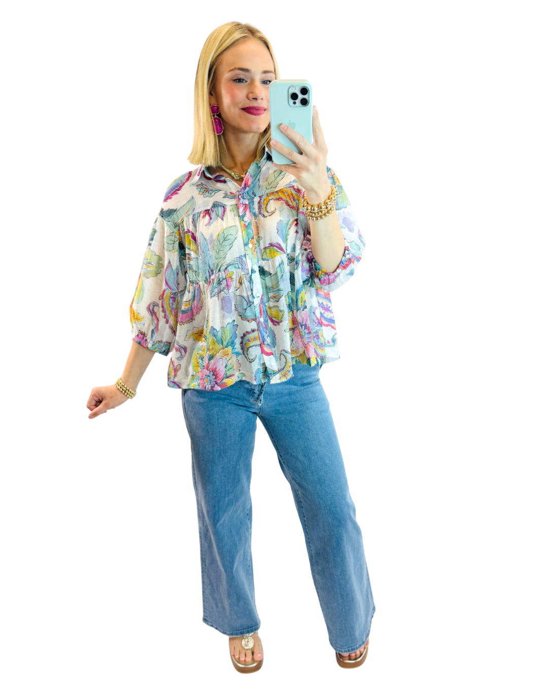 Woman wearing colorful floral print Luca top in mint with blue jeans, taking mirror selfie