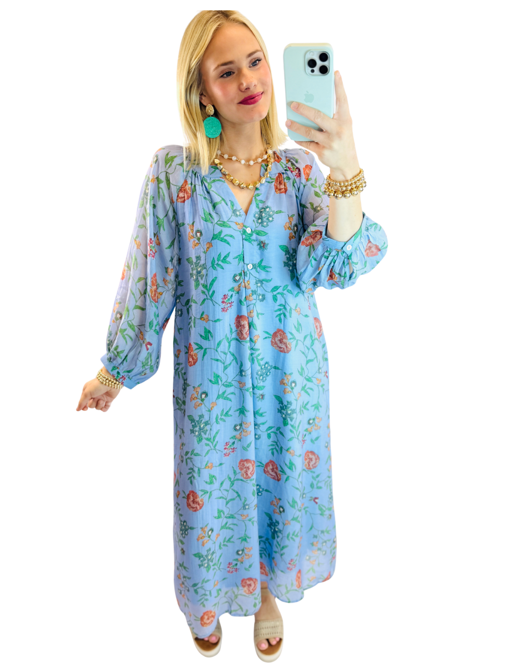 Woman wearing light blue floral maxi dress with long sleeves, taking mirror selfie with layered gold jewelry