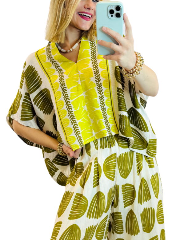 Woman wearing yellow and green palm leaf print top with matching bottoms, taking mirror selfie