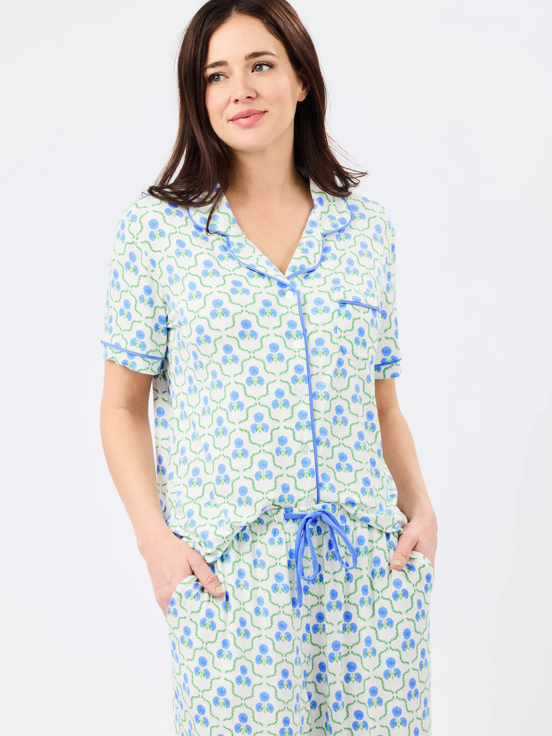 Woman wearing light blue floral patterned pajama set with short-sleeve button-up top and drawstring pants