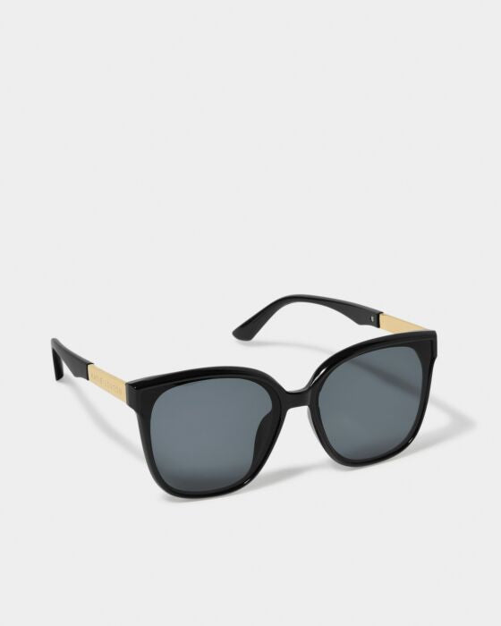Black cat-eye sunglasses with gold temple accents and dark tinted lenses on white background.