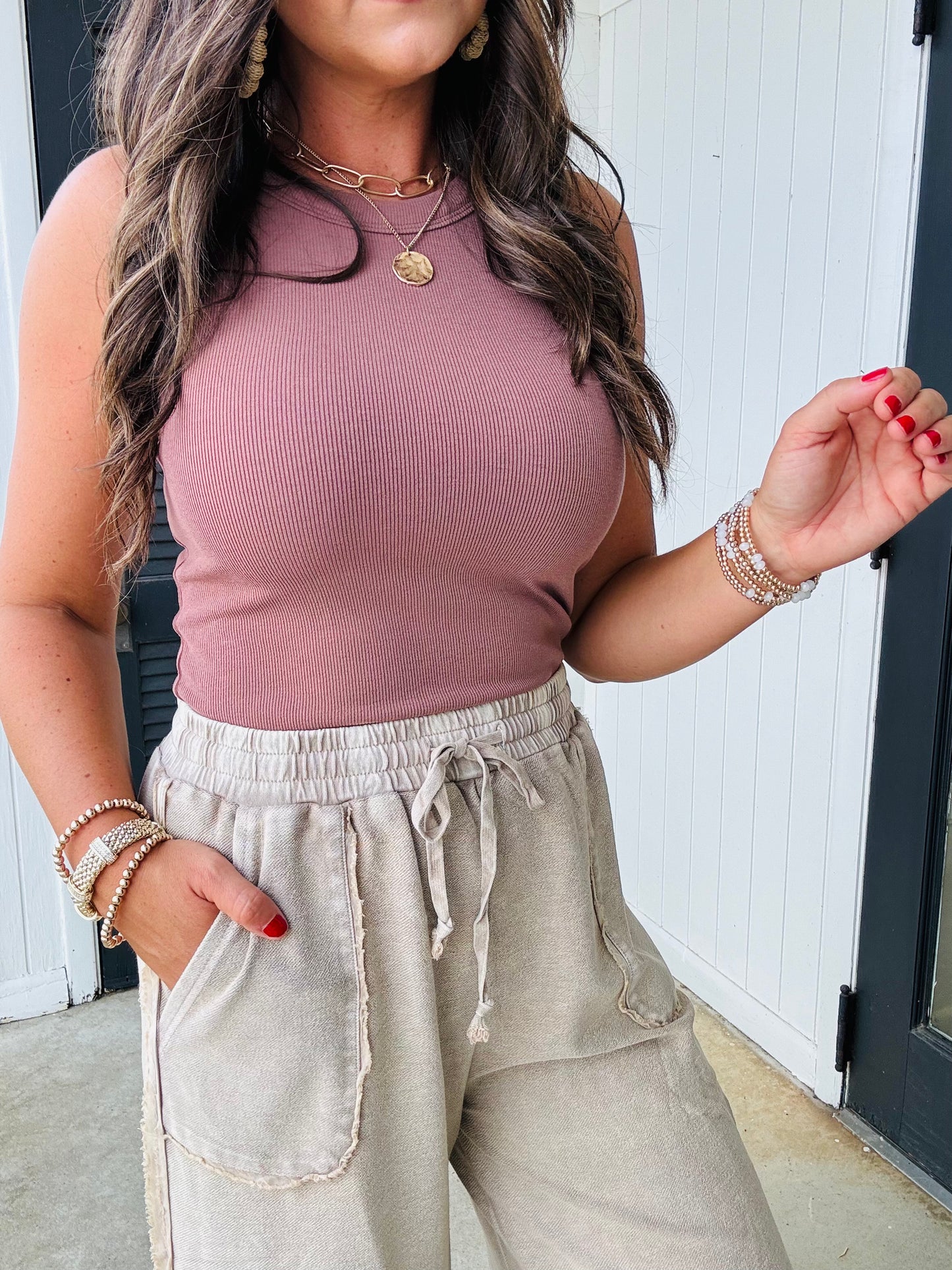 Woman wearing dusty rose ribbed tank top with beige drawstring pants and layered gold jewelry