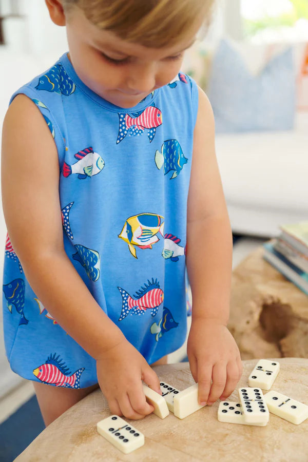 Young child wearing blue sleeveless bubble romper with colorful fish print while playing with dominos.