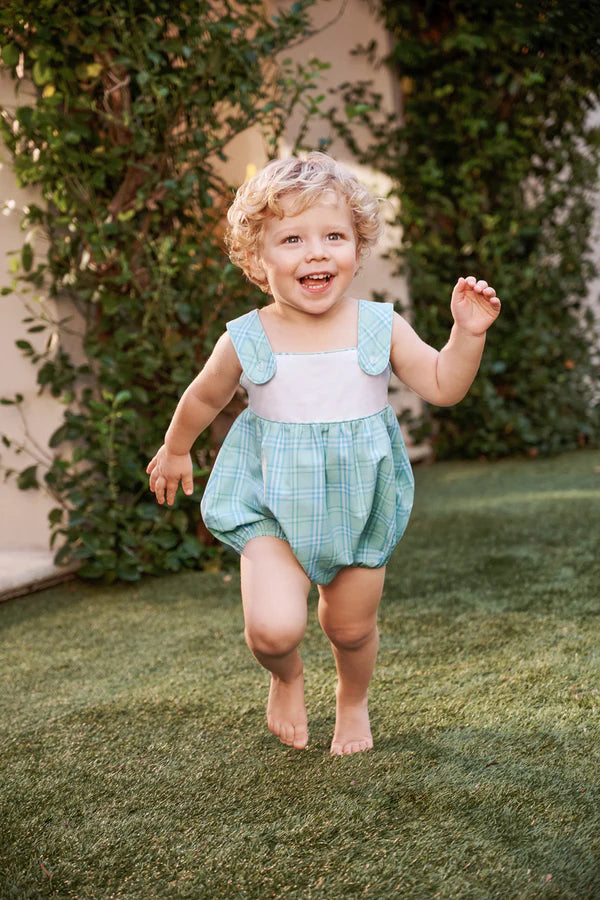 Happy toddler wearing light blue plaid Bingham Bubble romper running barefoot on grass