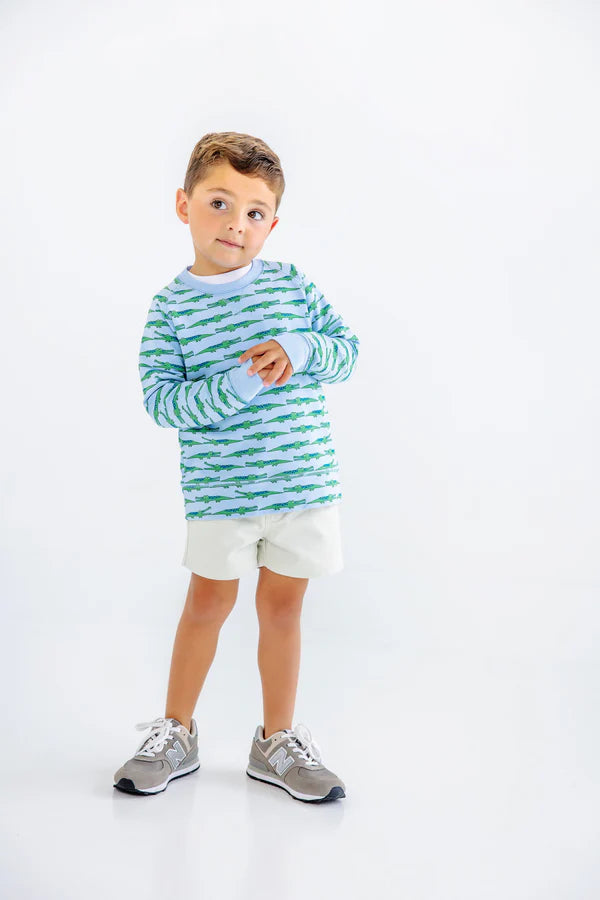 Young boy wearing green striped long-sleeve shirt and white shorts with gray sneakers on white background.