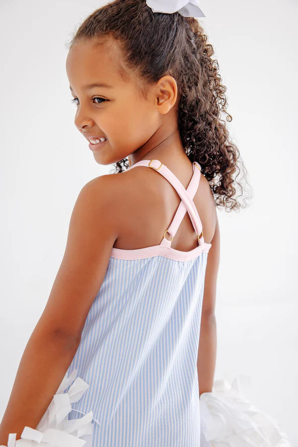 Young girl wearing light blue seersucker tennis dress with pink criss-cross straps and white bow details