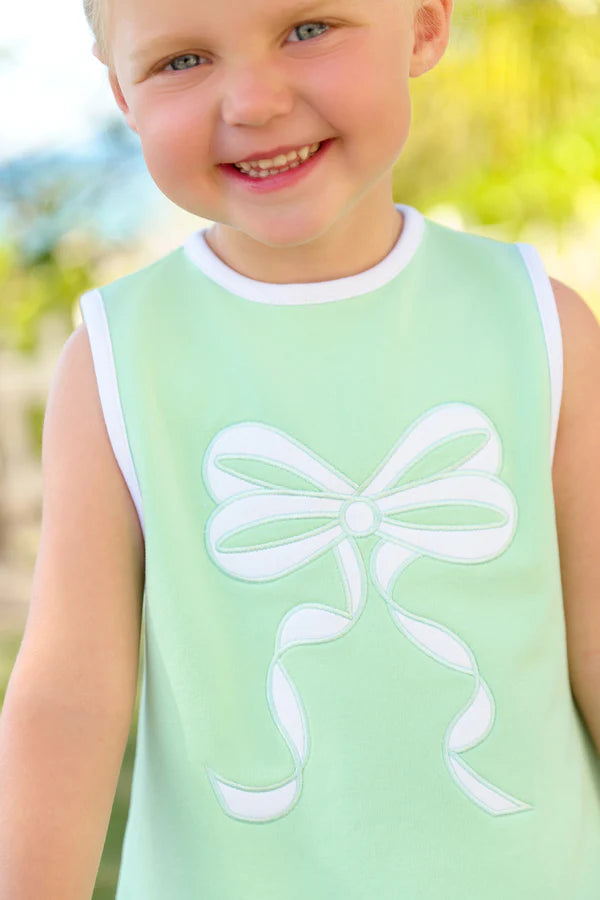 Young child wearing mint green sleeveless dress with white bow applique design, smiling outdoors