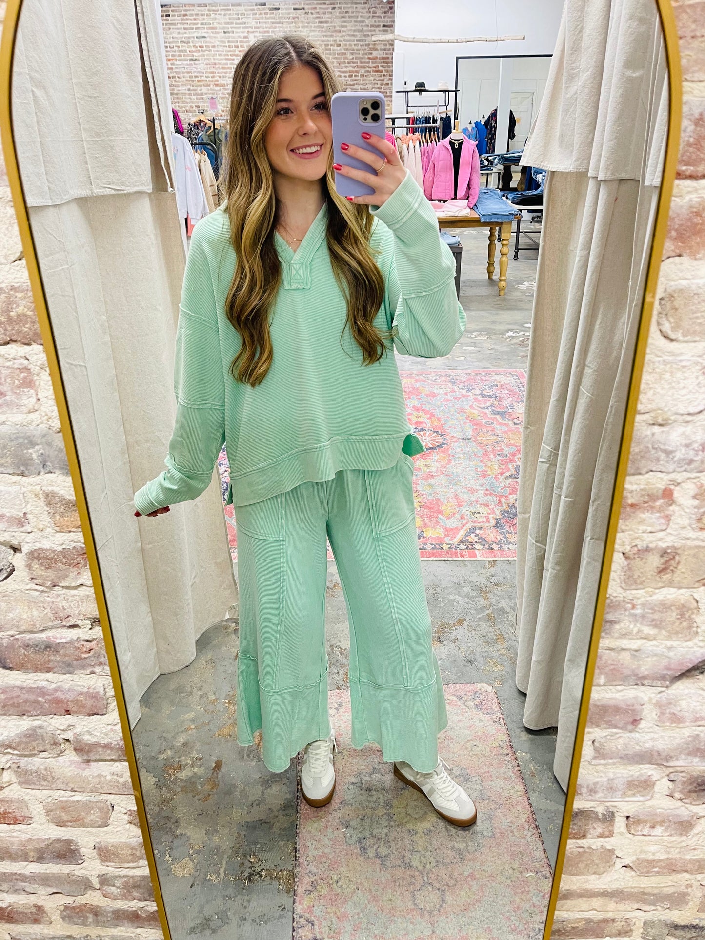 Woman wearing mint green cozy hoodie top taking mirror selfie in clothing store dressing room