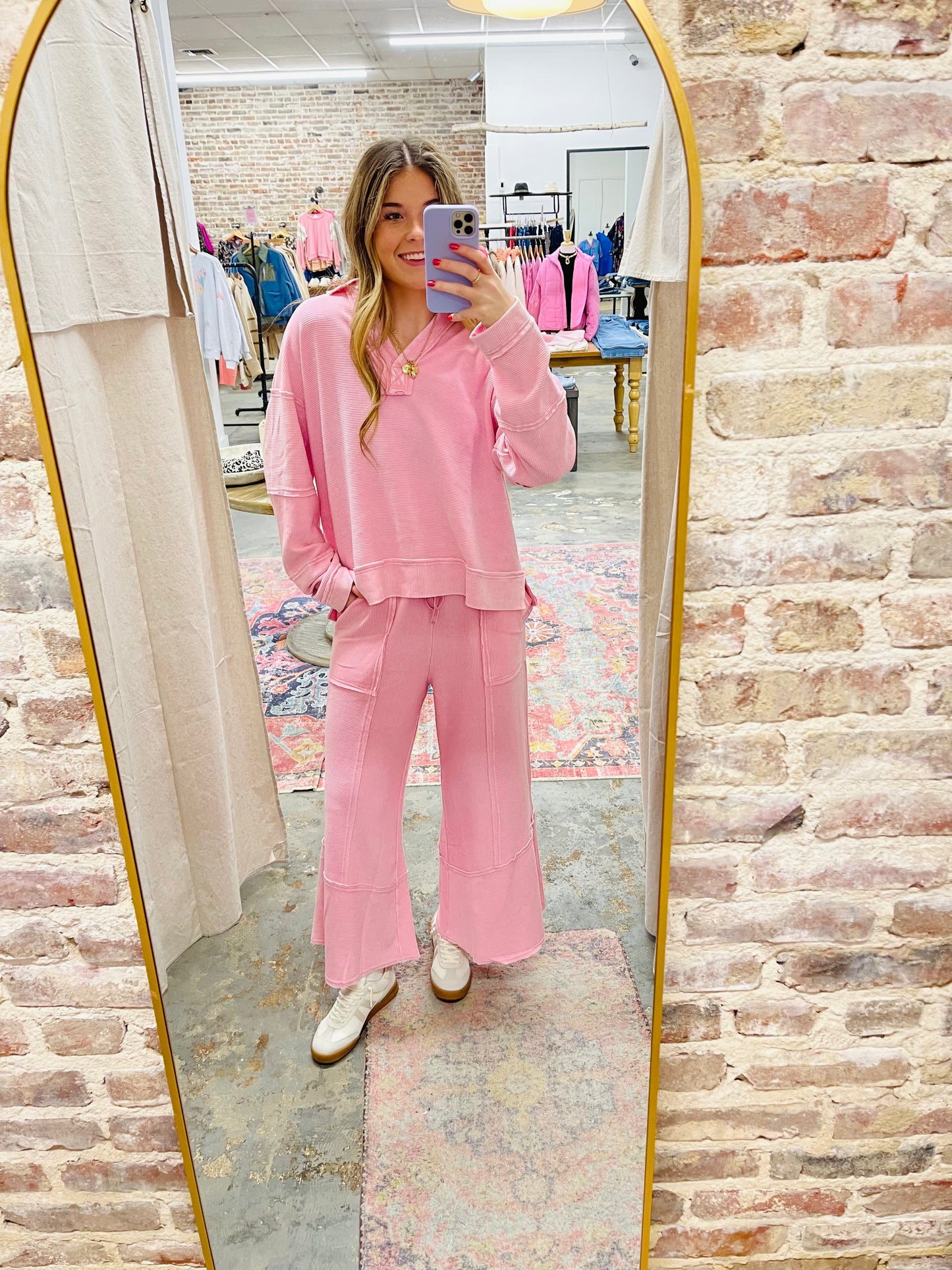 Woman wearing pink cozy long-sleeve top taking mirror selfie in clothing store dressing room