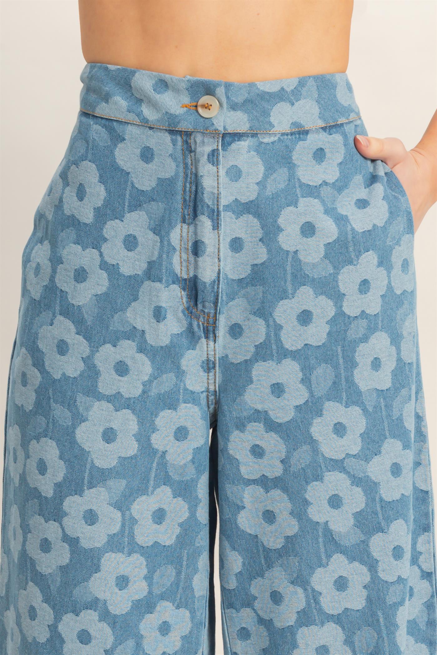 Blue denim pants with white floral pattern, high-waisted with button closure and front pockets.