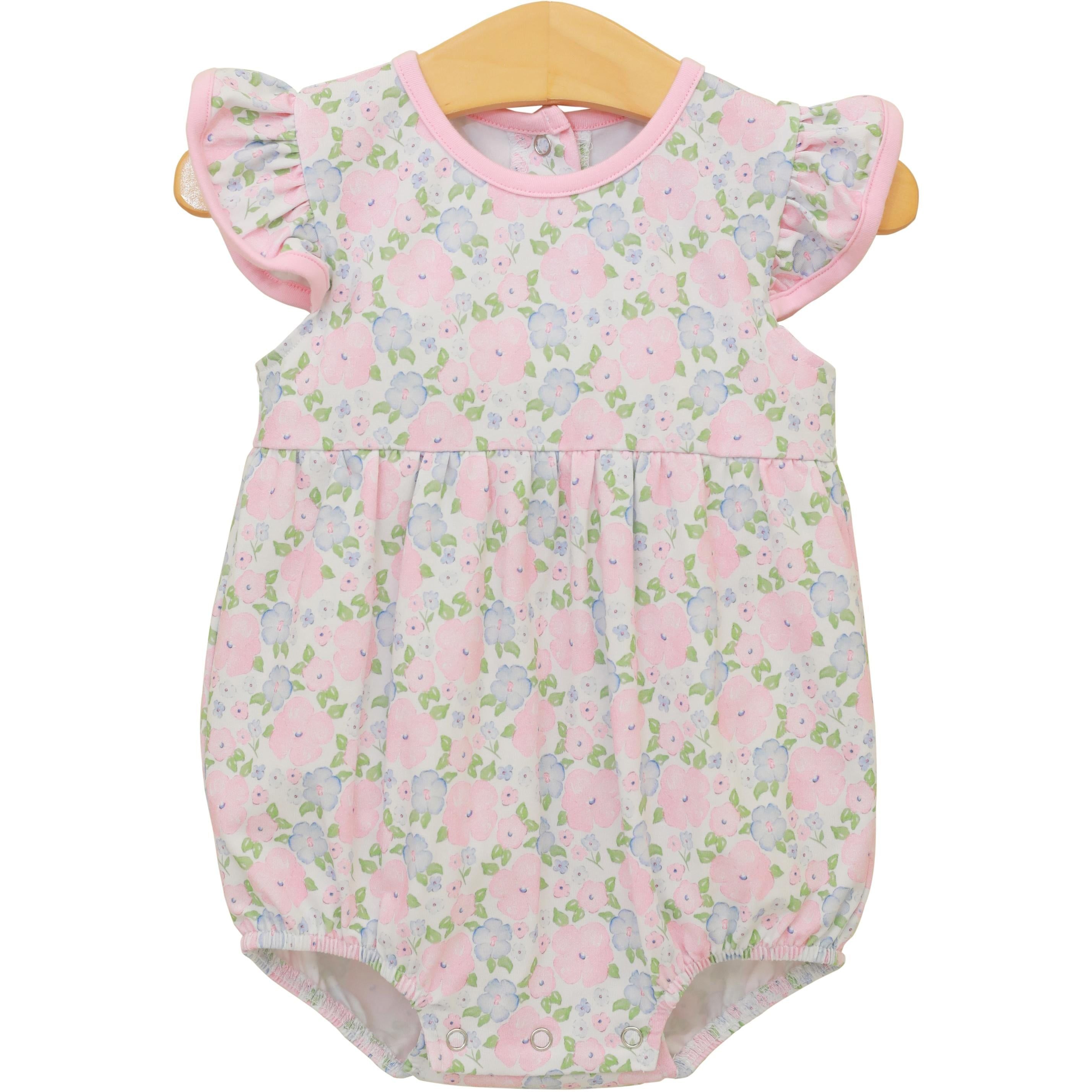 Baby girl floral bubble romper with pink trim, ruffled sleeves, and pastel flower print on wooden hanger.