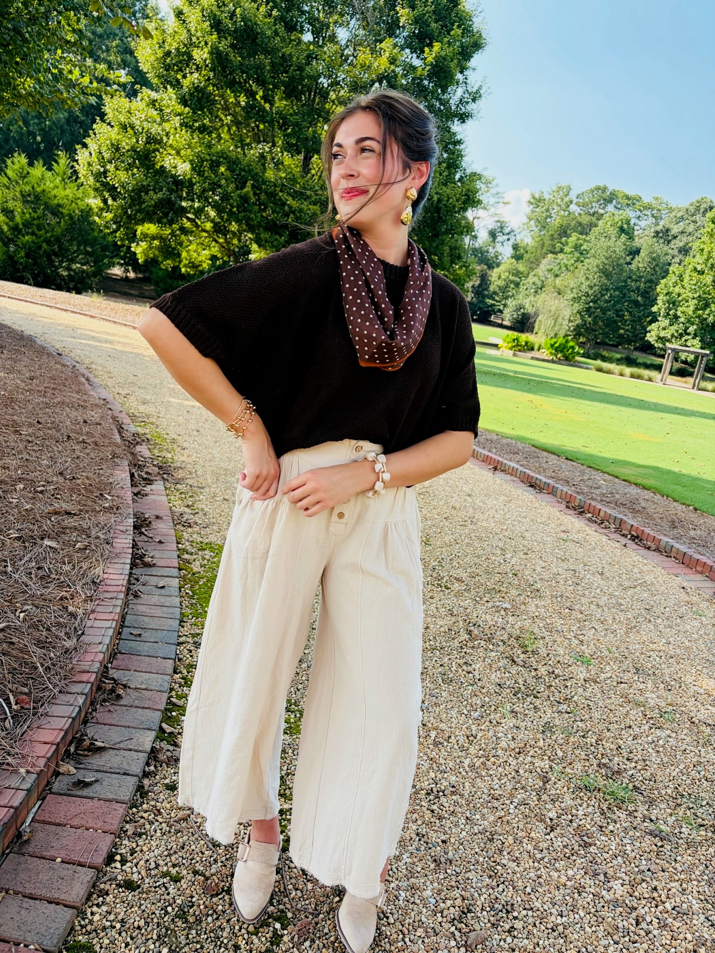 Lacey wearing the Kaia brown short-sleeve knit top with cream wide-leg pants and a polka-dot scarf