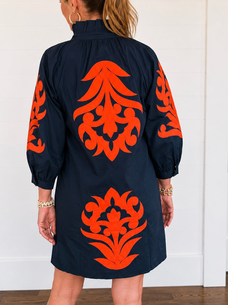 Bold burnt-orange appliqué medallions trail down the front, back, and full balloon sleeves of a crisp navy cotton shift, giving this easy silhouette a hand-finished, heirloom-embroidered look you won't find on a rack of basic tees and jeans.