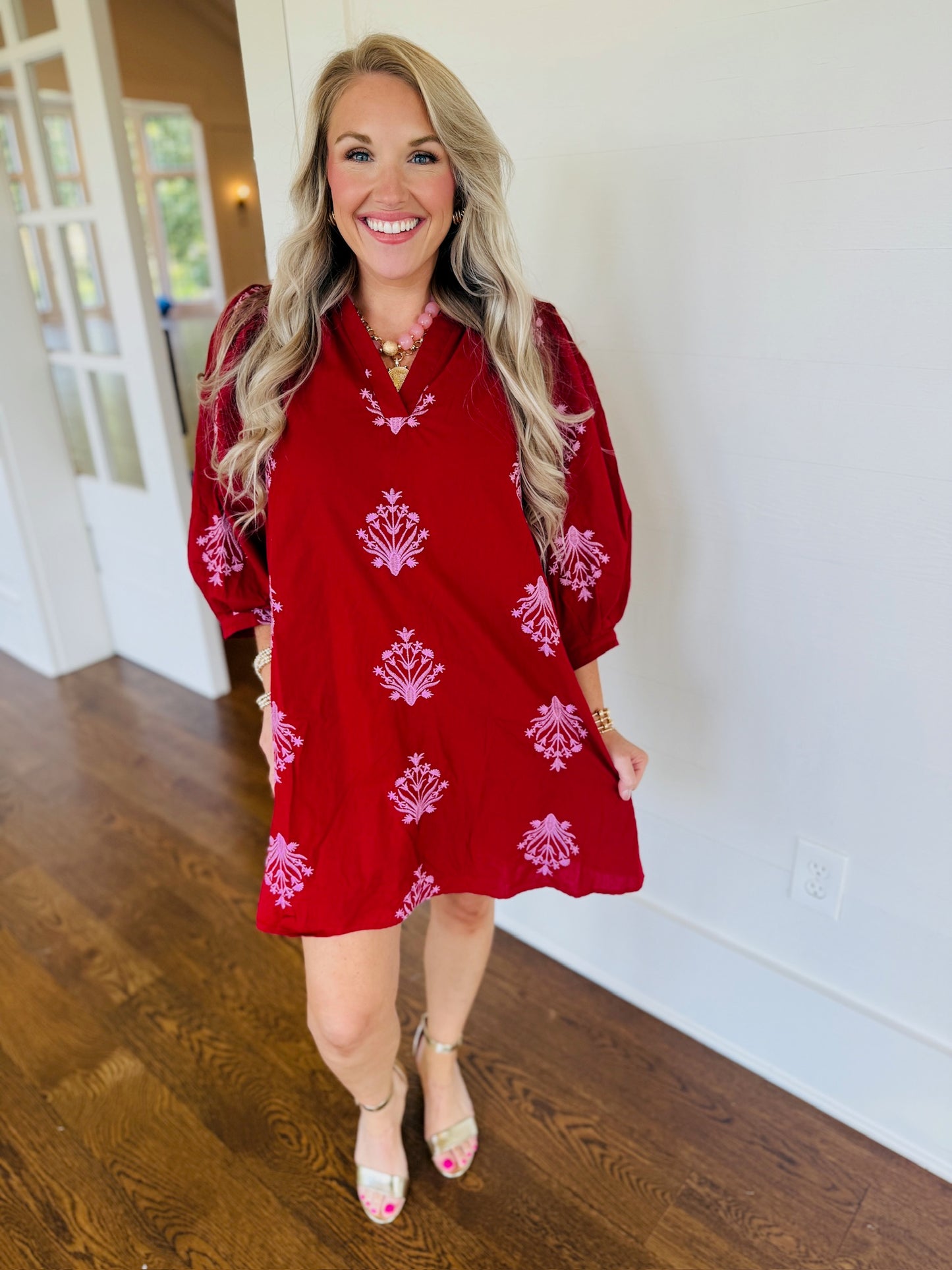 Model wearing a red 100% cotton fall dress with pink floral embroidery, V-neckline, three-quarter sleeves, and a relaxed fit.