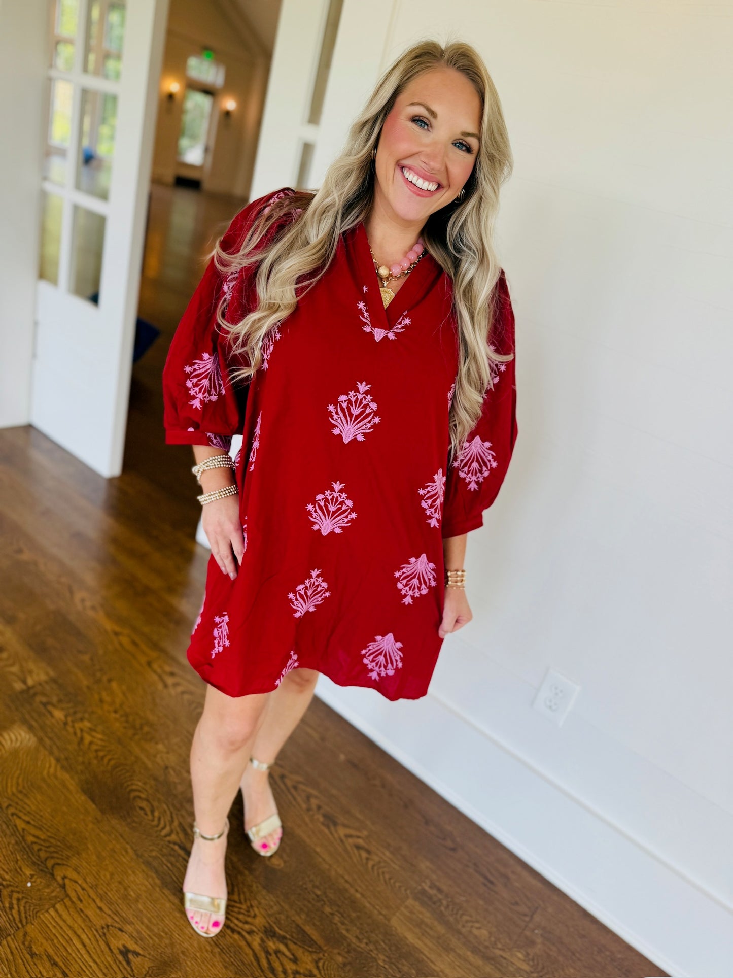 Woman wearing a red 100% cotton fall dress with pink floral embroidery, V-neckline, three-quarter sleeves, and a relaxed fit.