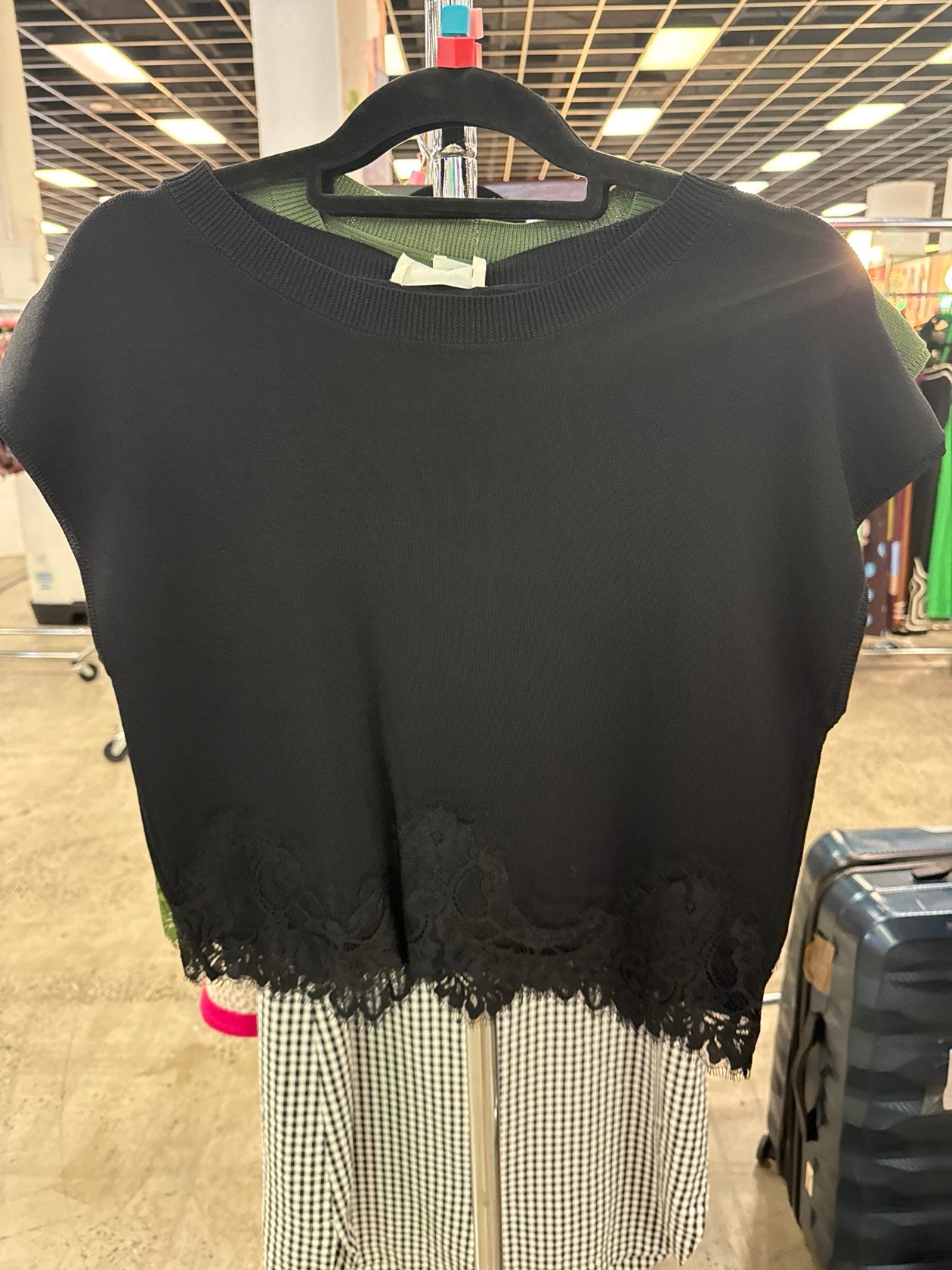Black sleeveless knit top with frayed hem detail hanging on store rack