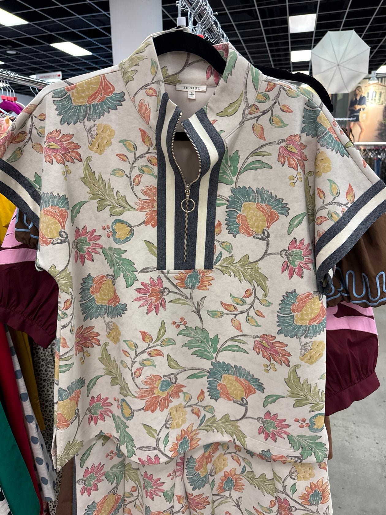 Jodifl oatmeal floral print short-sleeve top with navy striped zip-front neckline detail.