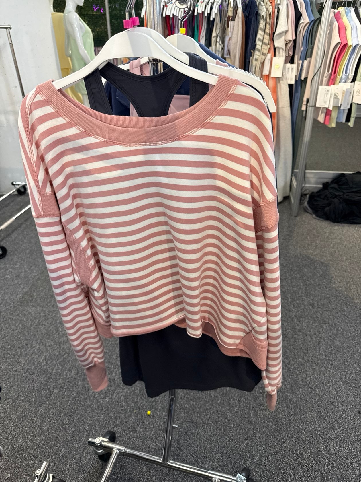 Pink and white horizontal striped long-sleeve crop sweatshirt displayed on a clothing rack.