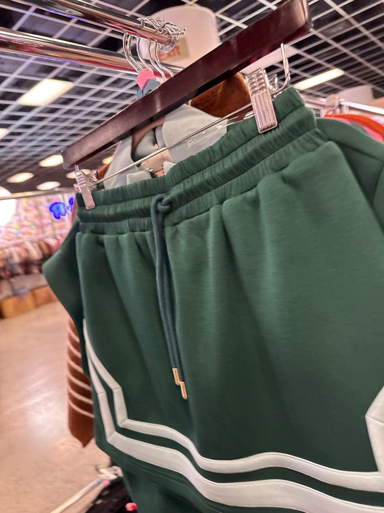Green drawstring athletic shorts with white stripe detailing along hem, displayed on wooden hanger in retail store.
