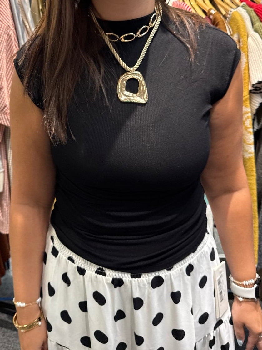 Woman wearing a fitted black sleeveless ribbed crew neck top with gold layered necklace.