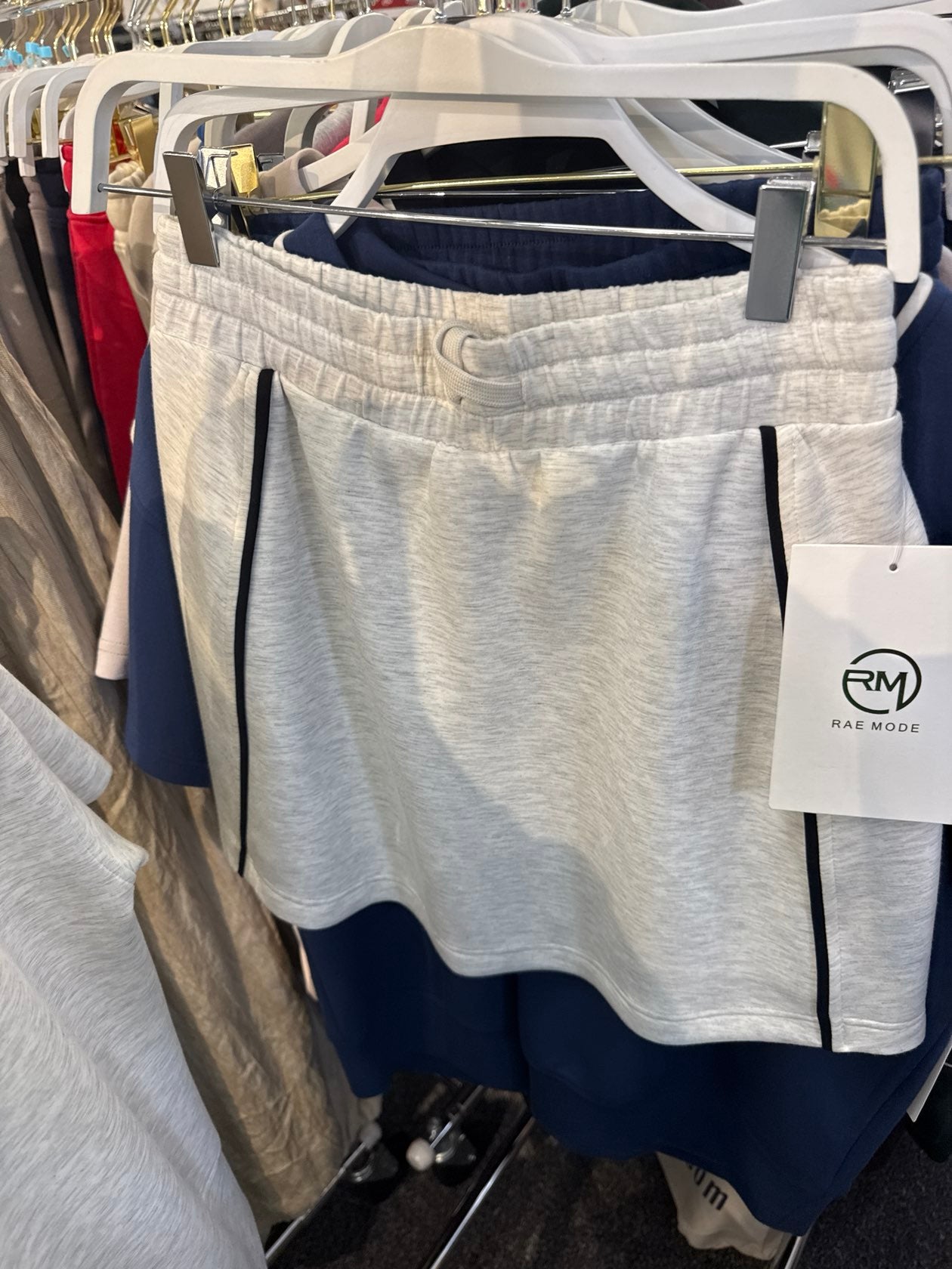 Light heather grey athletic shorts with black piping trim and elastic waistband, displayed on hanger.