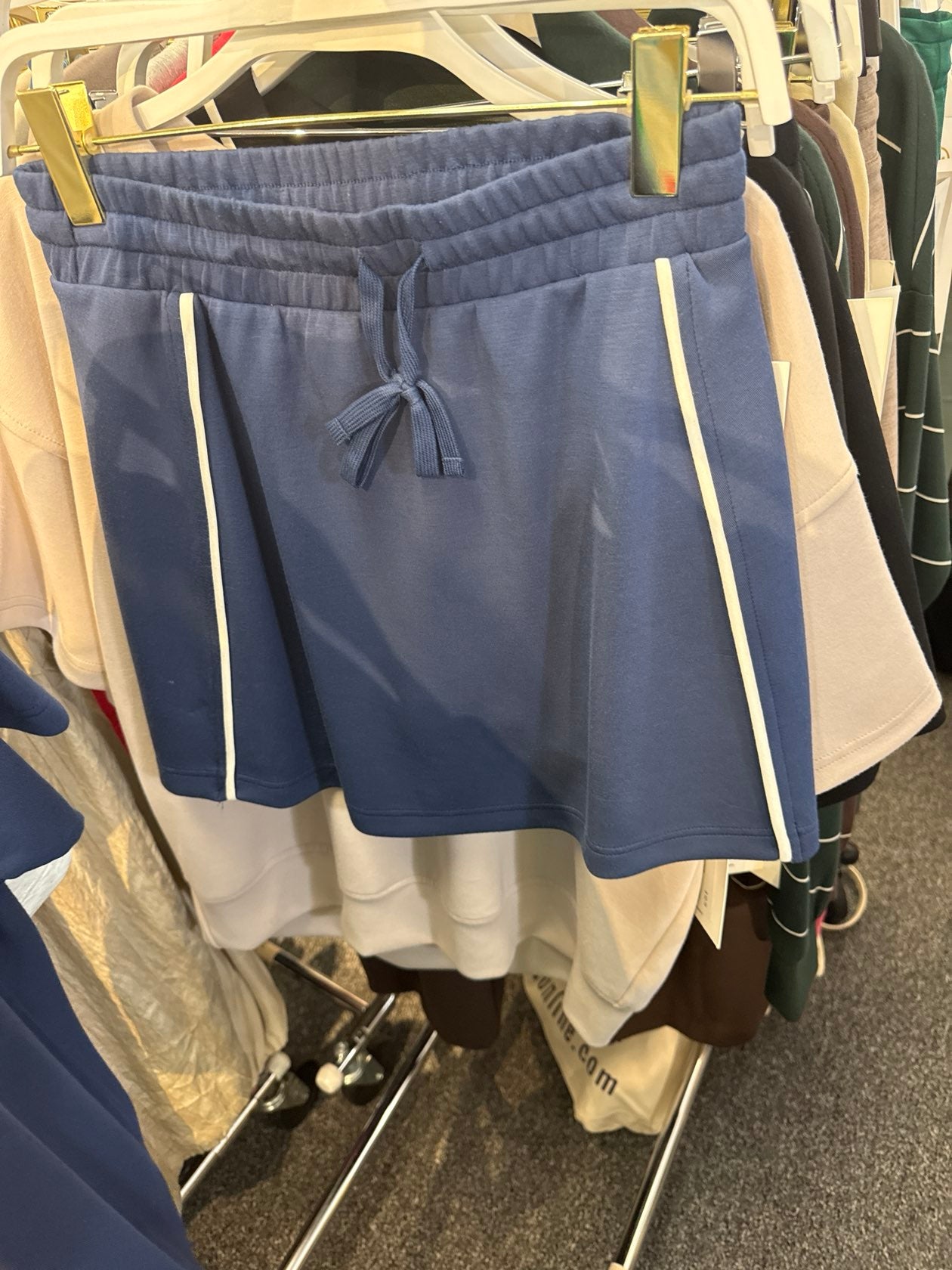 Smoky navy blue drawstring shorts with white side stripe piping detail, displayed on clothing rack.