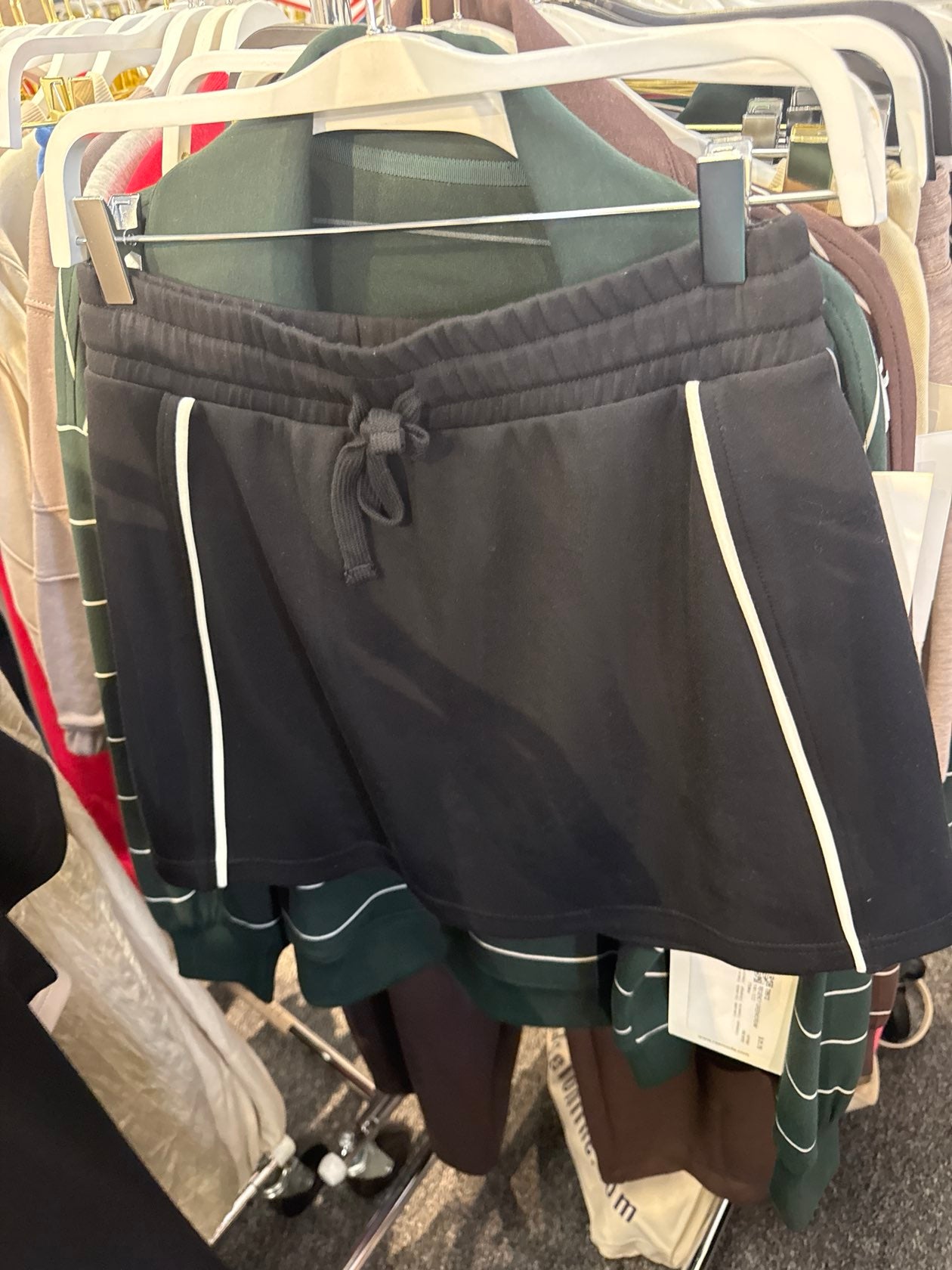 Black drawstring athletic shorts with white side stripe detailing and green color-block hem trim.