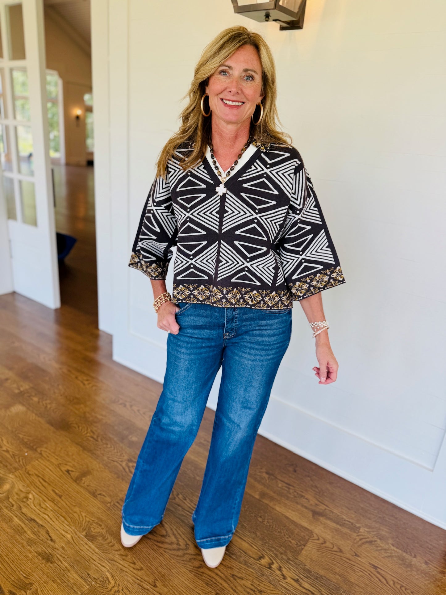 Model wearing GIGIO Rylee espresso and ivory geometric print v-neck top with blue wide-leg jeans and white heels