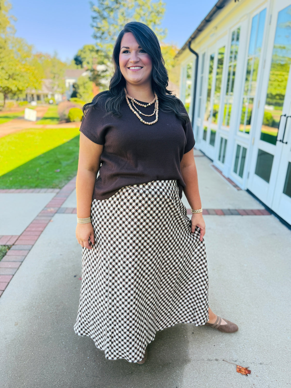 Alex wearing the Ada brown waffle knit short sleeve top in extended sizing with a brown-and-cream gingham midi skirt.