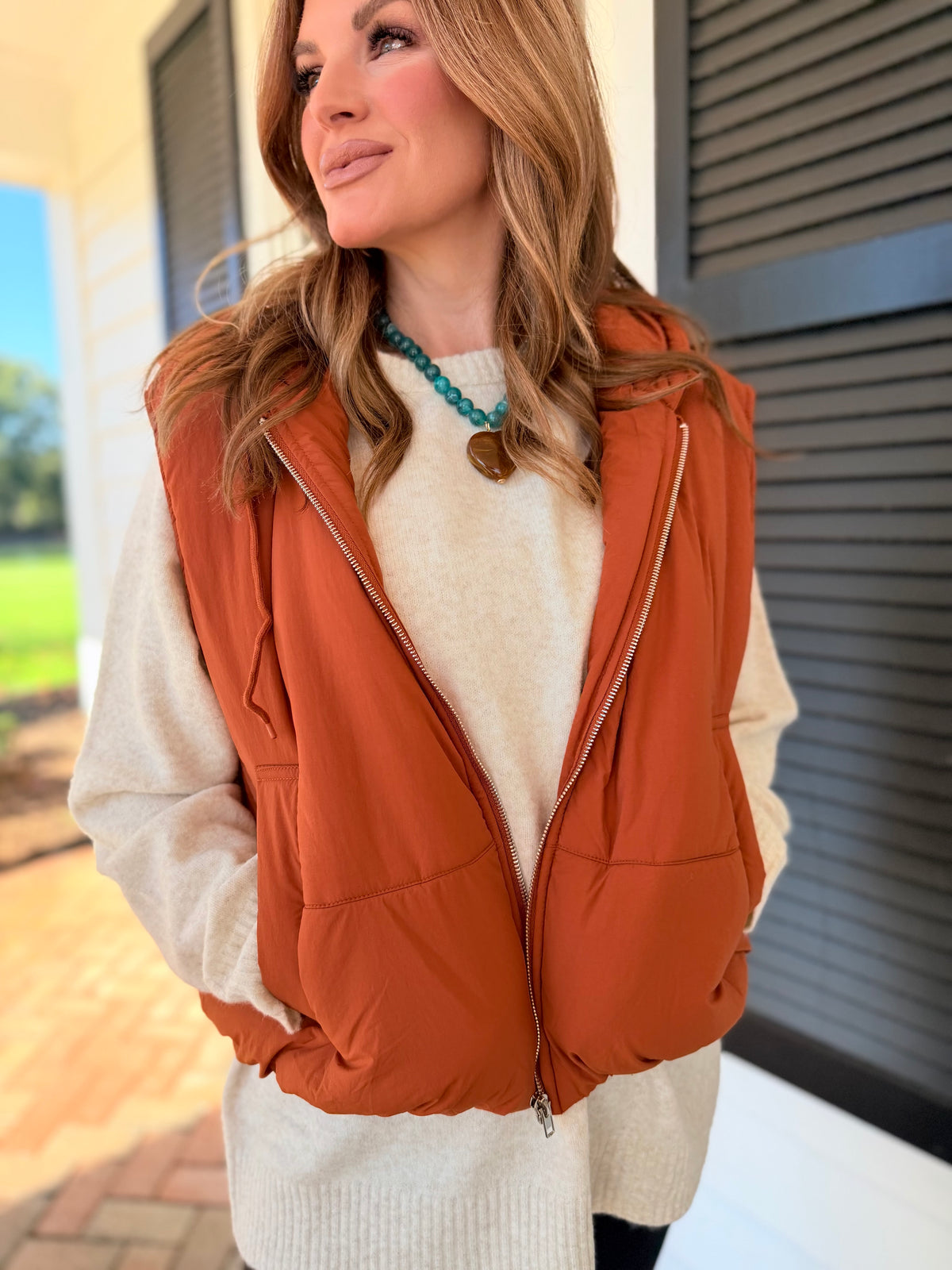 Close-up of the Autumn rust puffer vest showing its attached hood, zip-front closure, side pockets and padded texture.