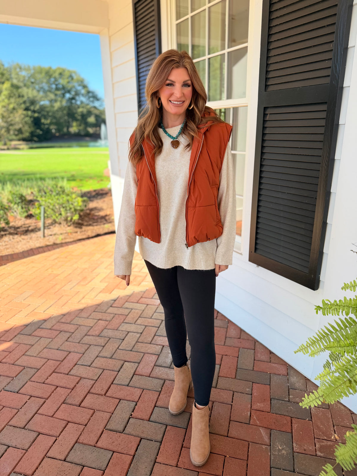 Morgan wearing the Autumn rust hooded puffer vest over a cream sweater with black leggings and neutral ankle boots.