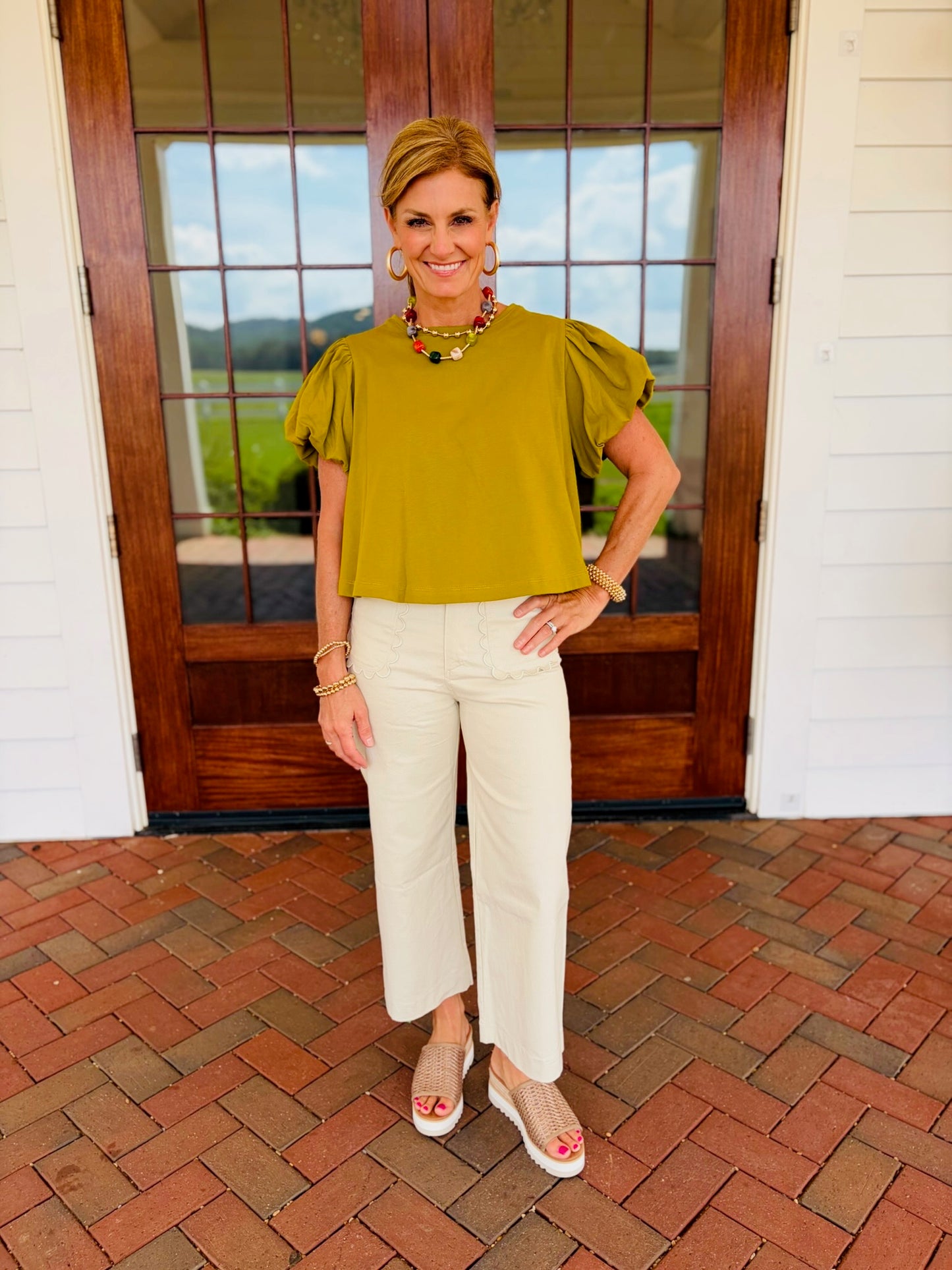 Back view of Ginny wearing the Brittany martini olive puff-sleeve cotton top with cream cropped pants