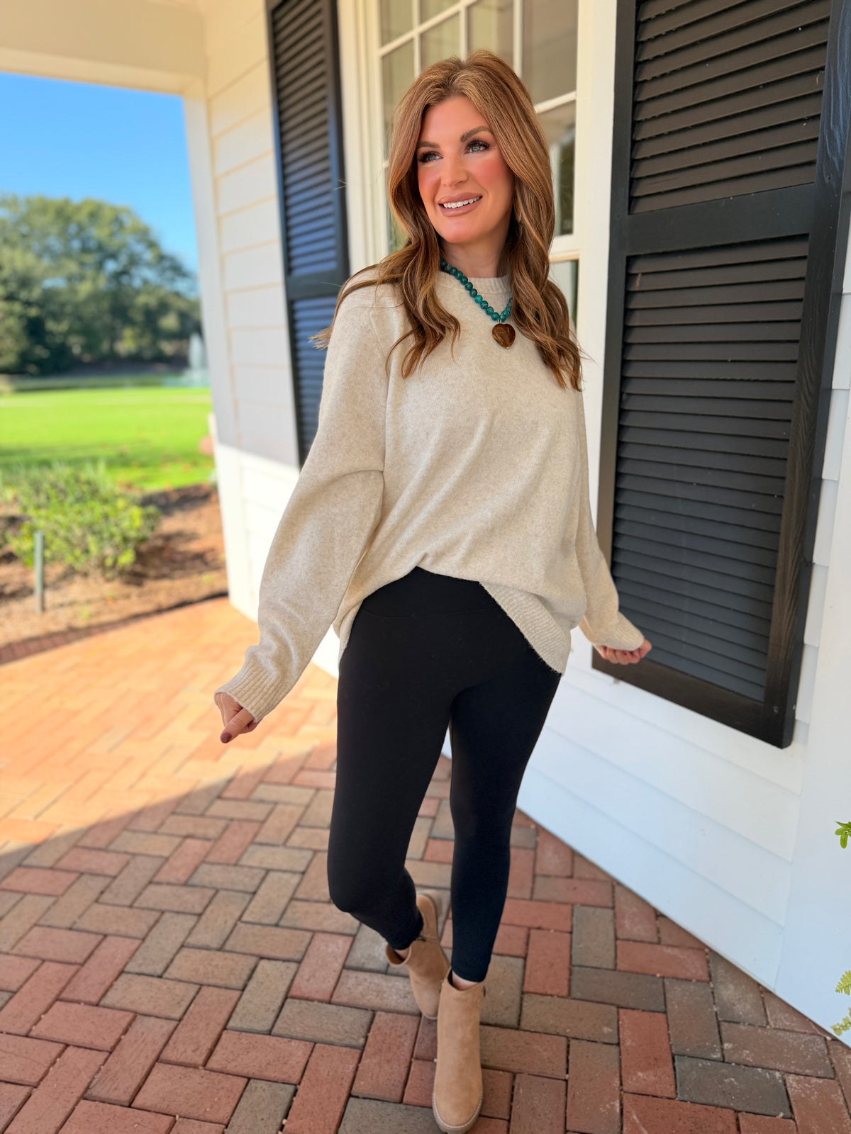 Morgan wearing the Corinna oatmeal oversized crewneck sweater with black leggings and taupe ankle boots.