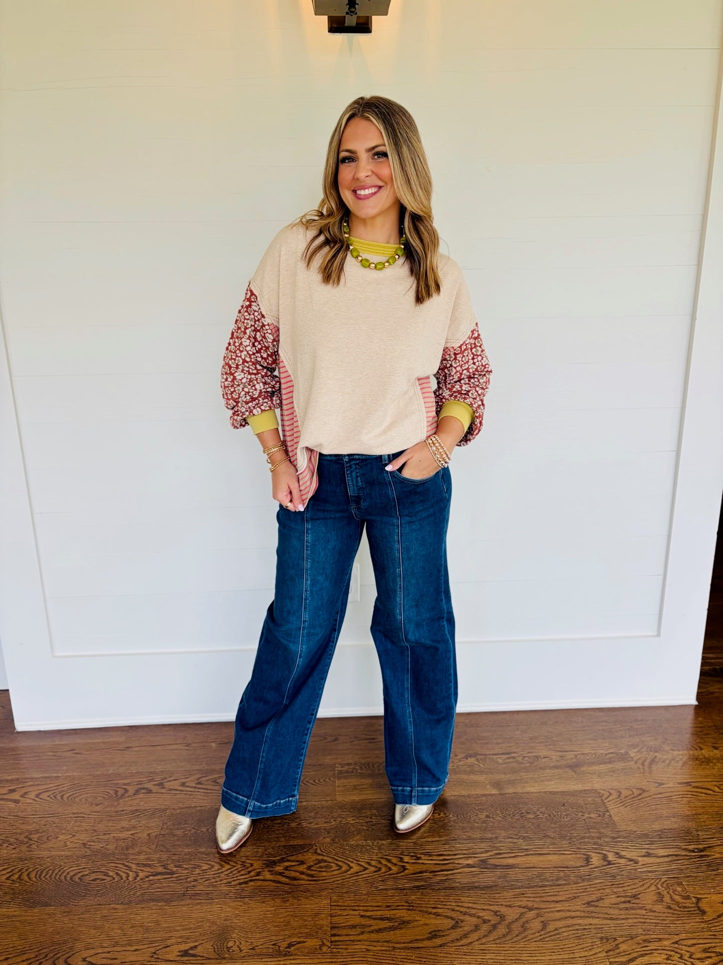 Full-length view of Jessica wearing the Delaney oatmeal patchwork sweatshirt with patterned sleeves and jeans