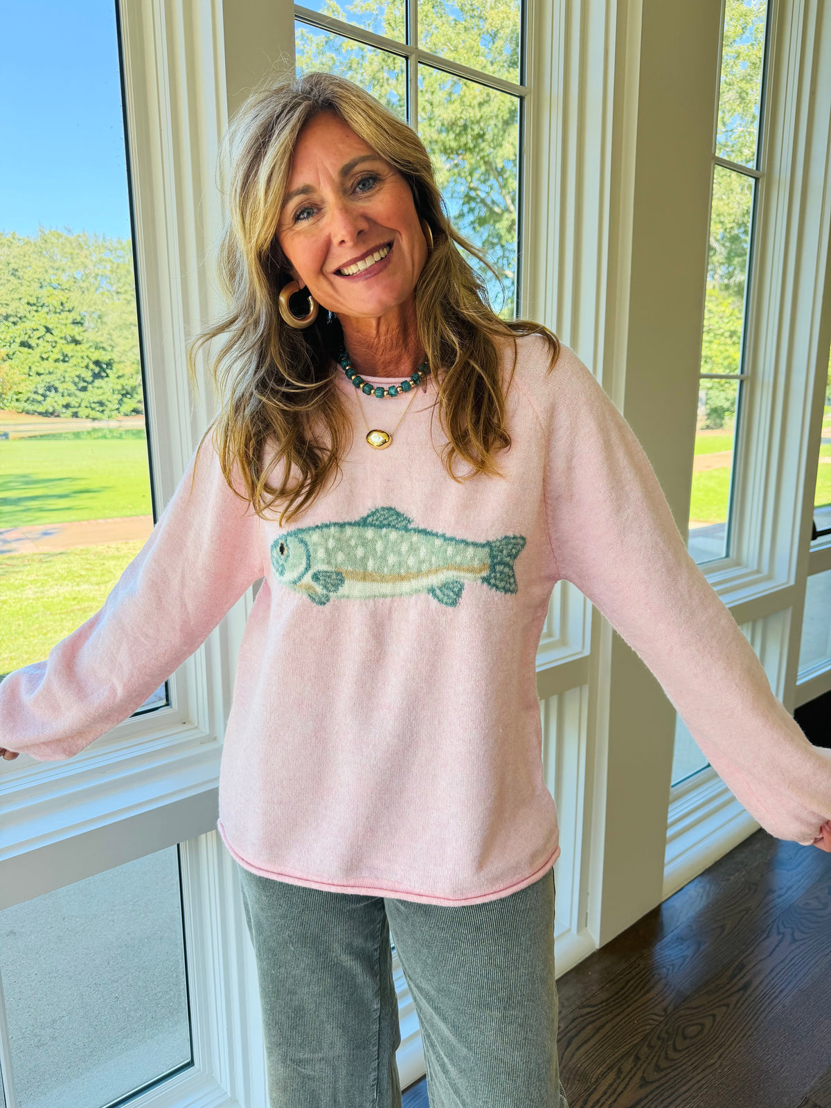 Kelly wearing the Delaney pink knit sweater, showing its green fish graphic, round neckline and relaxed long sleeves.