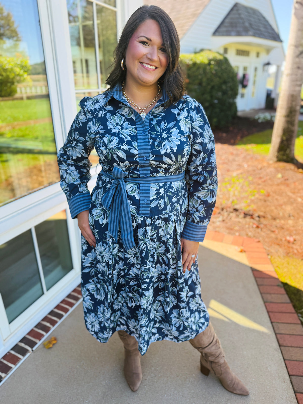 Alex wearing the Estelle blue floral print midi dress with its striped tie belt and neutral knee-high boots.