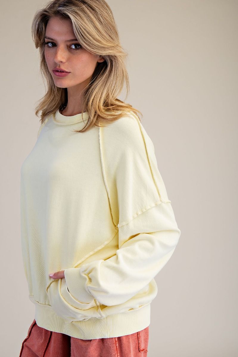Woman wearing oversized pale yellow Marigold pullover sweatshirt with ribbed cuffs and hem, paired with coral pants.