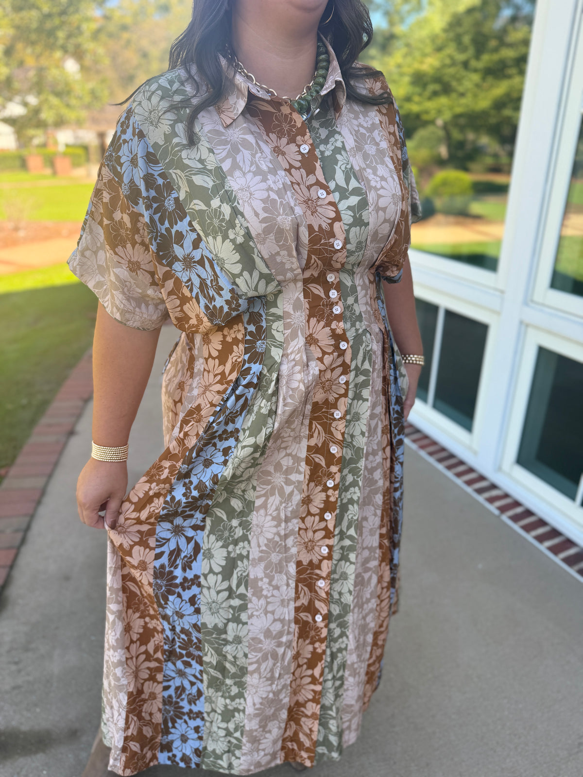 Close-up of the Faith floral maxi dress showing its collar, button front, waist pleats and vertical floral bands in brown, beige, green and blue.