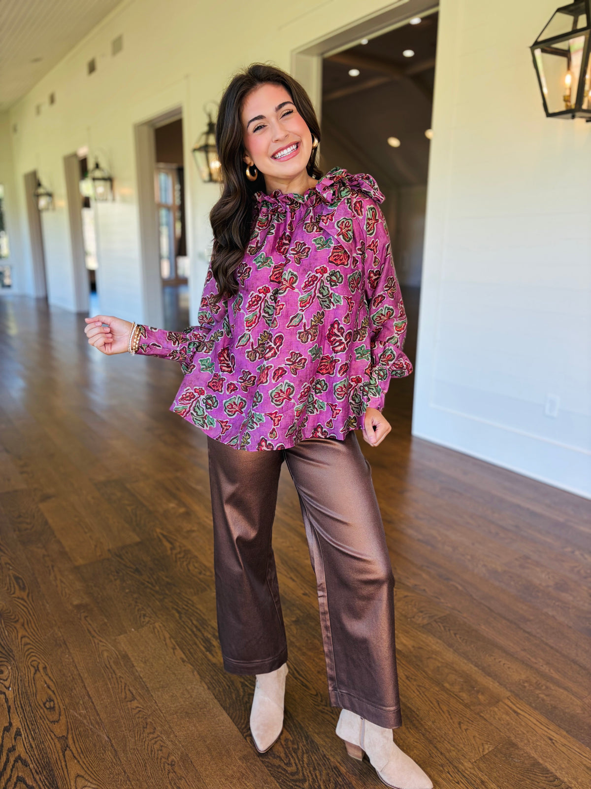 Lacey wearing the Harper pink floral ruffle blouse with brown trousers and neutral ankle boots.